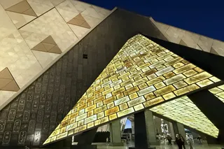 大埃及博物館入口的三角形天窗,金色光線灑在刻滿象形文字的巨大石牆上